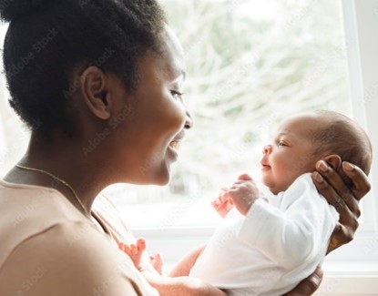 A smiling woman holds a newborn in front of her face.