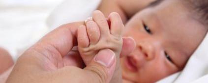 A newborn baby holds an adult hand