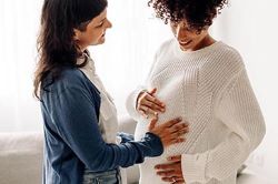 woman touching another woman's pregnant stomach