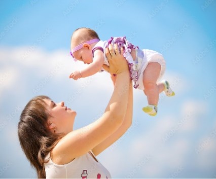 A woman holds a baby above her against a blue sky.