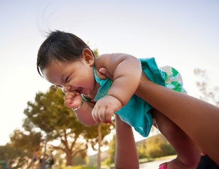 A laughing infant is held up by two arms.