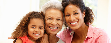 A young child, an older woman, and a middle-aged woman look at the camera, smiling