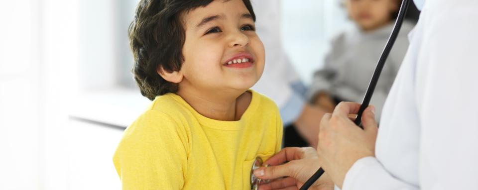 A boy smiles while a doctor listens to his chest with a stethoscope.