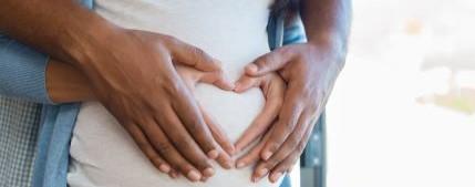 Two sets of hands form a heart shape over a pregnant belly.